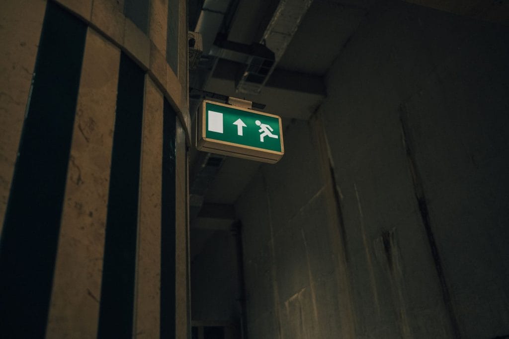 Green and white emergency exit sign hanging from a metal bar